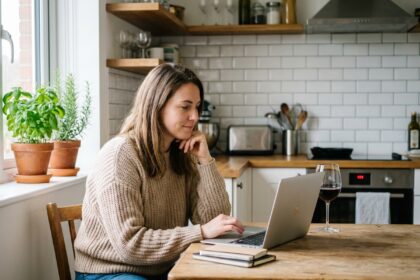 Femme en sweater beige regardant des bouteilles de vin sur son ordinateur
