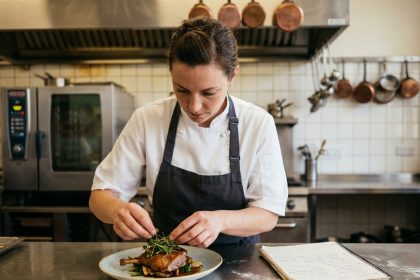 Femme adulte en veste de chef plaquant un plat dans une cuisine de formation professionnelle pendant une formation CAP cuisine